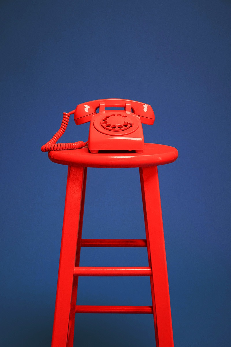 rotes Telefon steht auf einem roten Hocker vor einem blauen Hintergrund